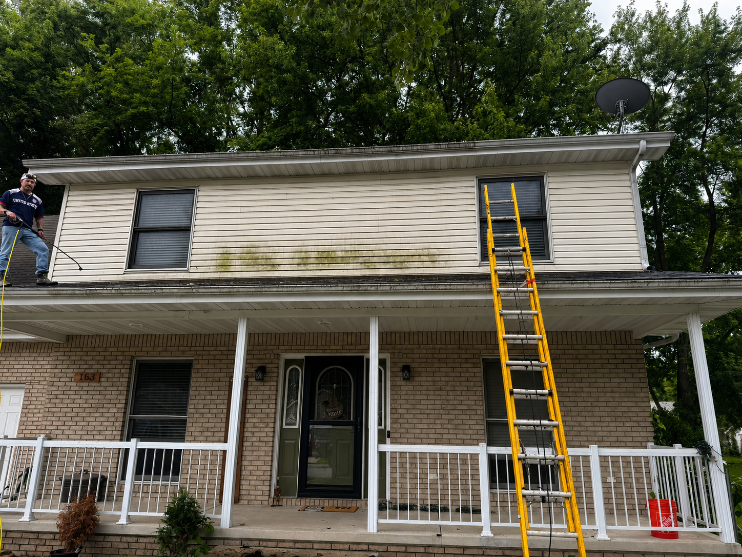Front of house with algae buildup on upper siding before cleaning